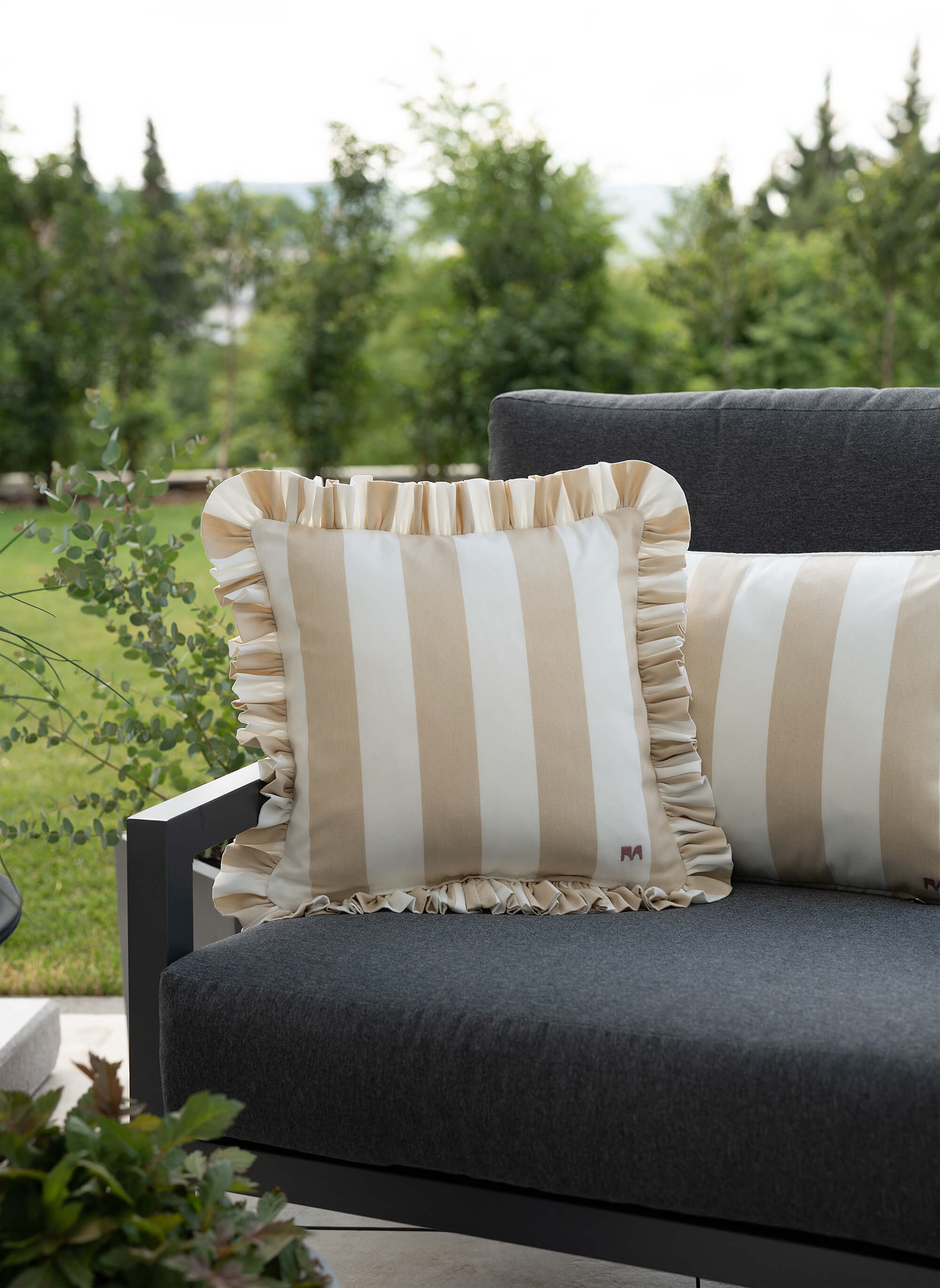 another mondaen Outdoor Kissen Ruffled Charm Beige auf Gartenlounge – beigen-weiß gestreifte Designkissen für Terrasse und Garten aus der VACANCES Outdoor Kollektion