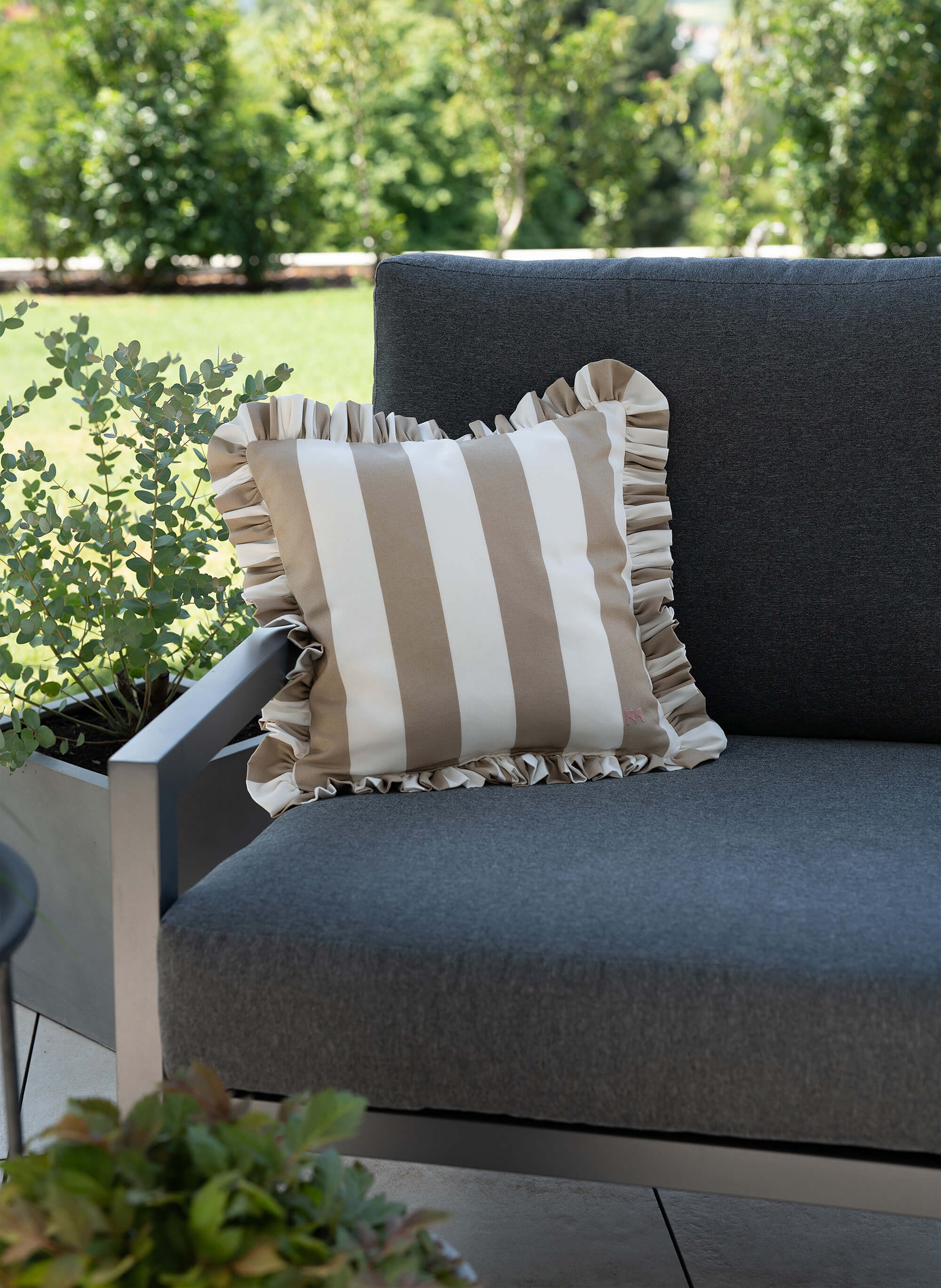 another mondaen Outdoor Kissen Ruffled Charm Taupe auf Gartenlounge – Taupe-weiß gestreifte Designkissen für Terrasse und Garten aus der VACANCES Outdoor Kollektion